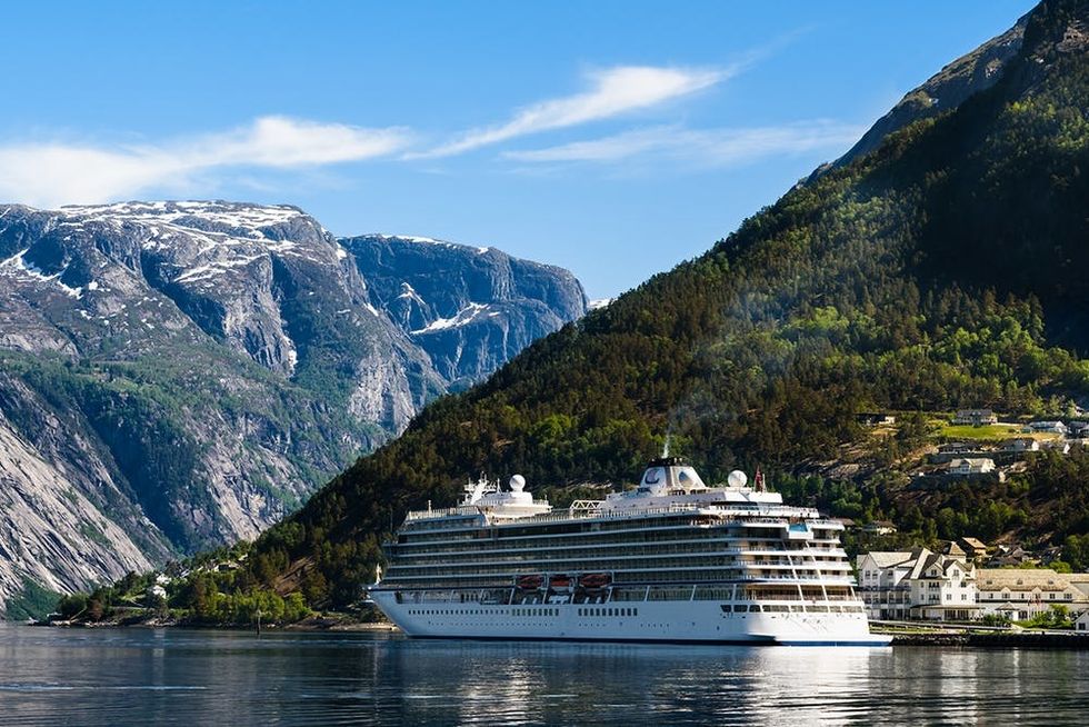Eidfjord, Norway - May 21, 2018: Travel documentary of everyday life and place. The cruise ship Viking Sun visiting the village on a sunny and calm day. Mountain peaks in the background.