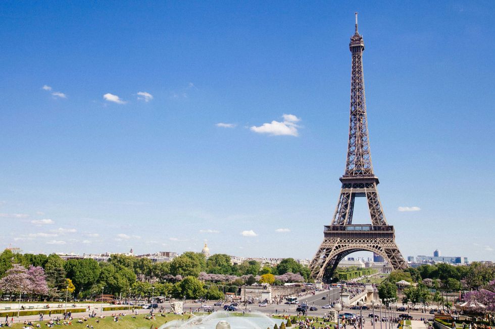 Eiffel Tower under clear blue sky, surrounded by lush greenery and park visitors.