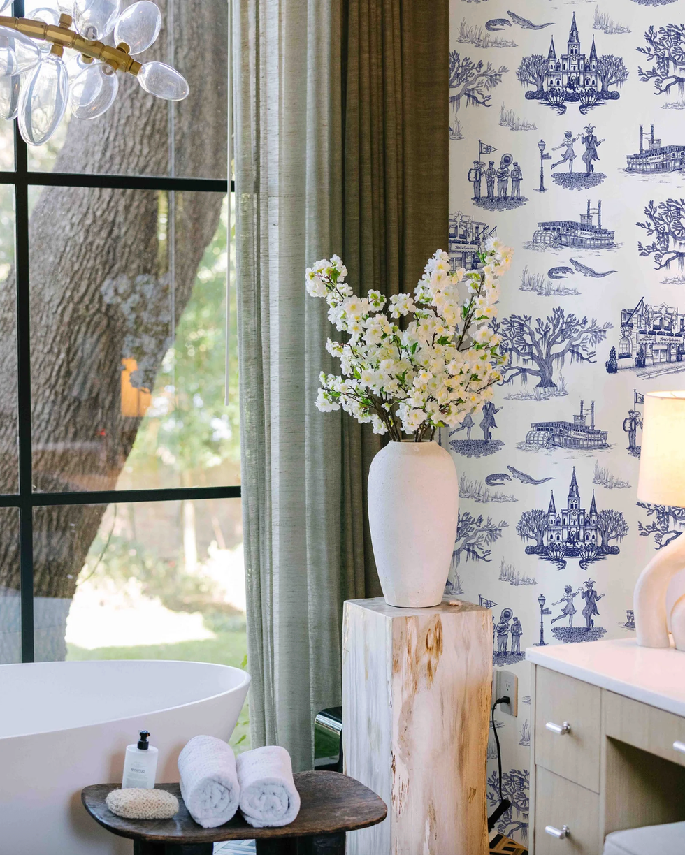 Elegant bathroom with floral vase, scenic wallpaper, and large window overlooking a tree.
