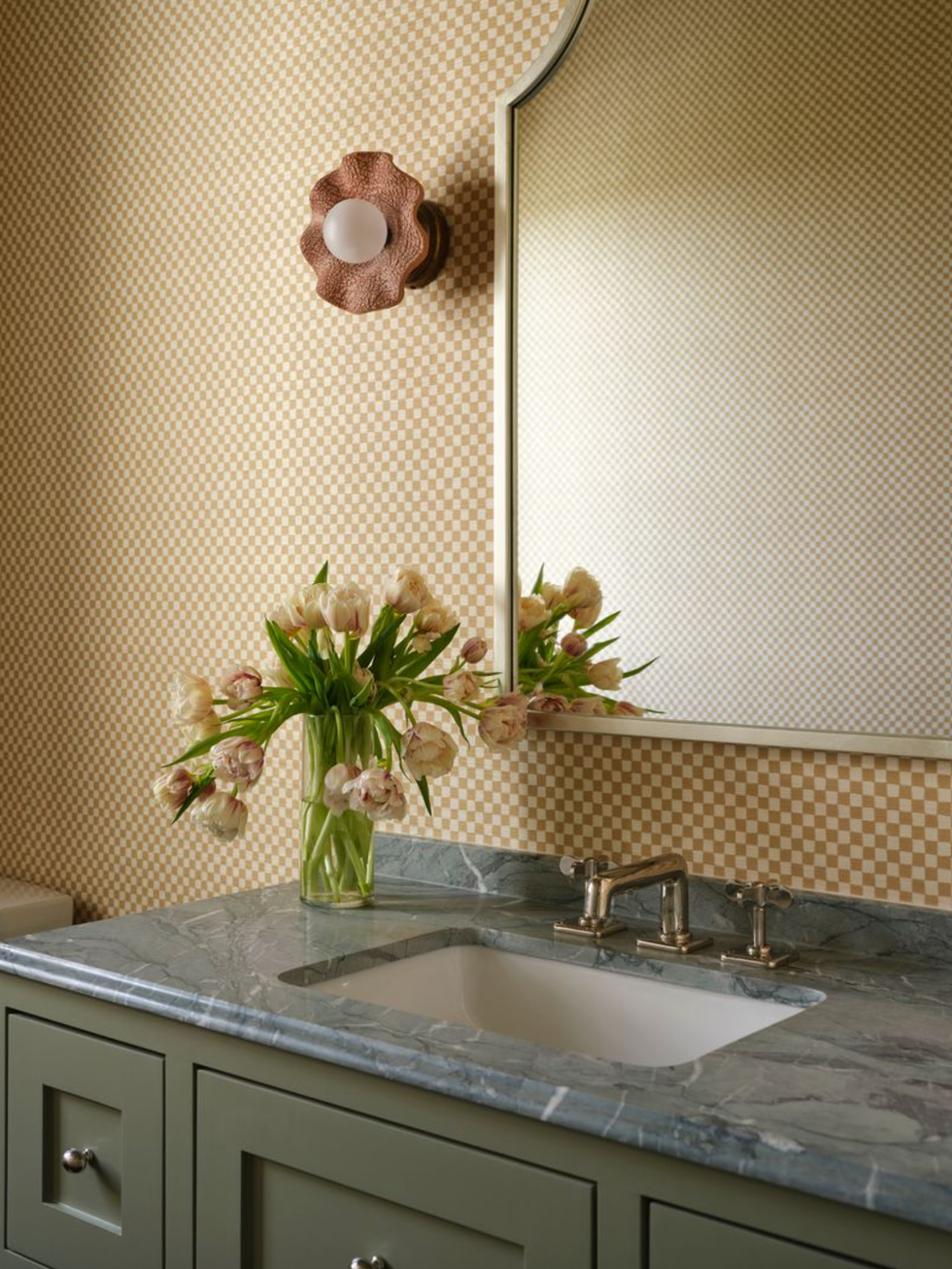 Elegant bathroom with tulips, green vanity, marble countertop, mirror, and wall sconce.