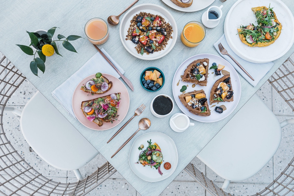 Elegant brunch spread with waffles, toast, salads, and drinks on a light blue table.
