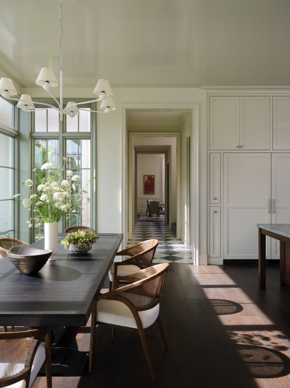 Elegant dining area with large windows, dark table, chairs, and chandelier, leading to a hallway.