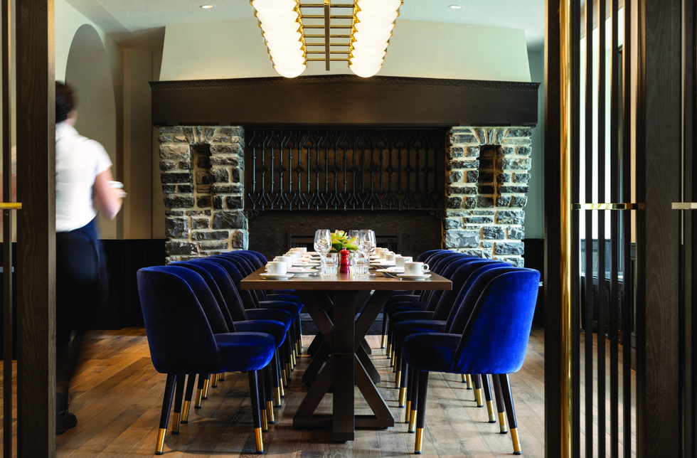Elegant dining room with blue velvet chairs and a set table, server passing by.