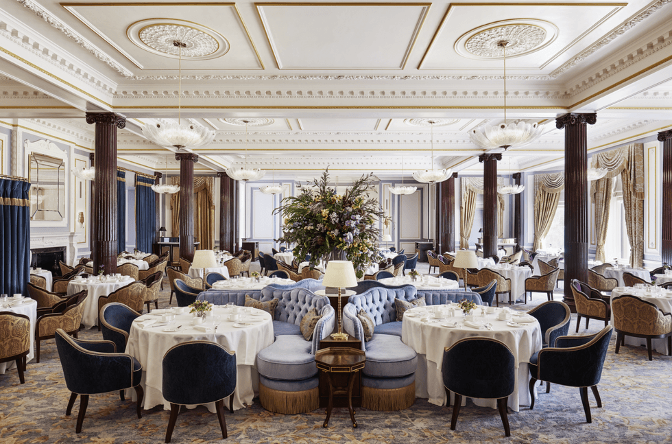 Elegant dining room with chandeliers, round tables, plush chairs, and a decorative ceiling.