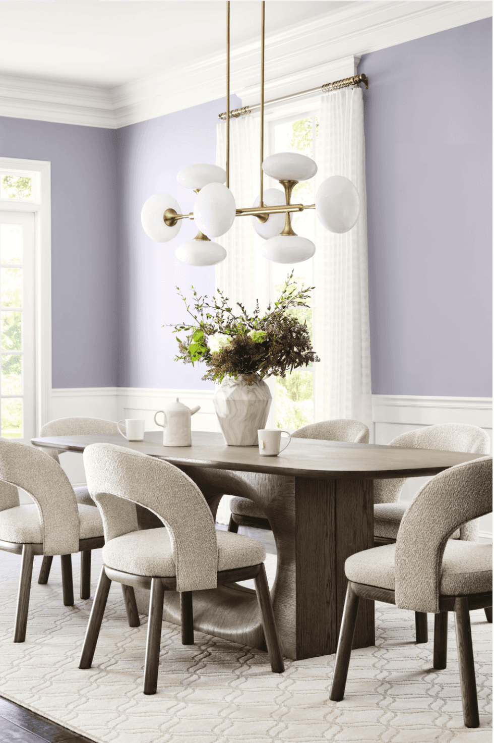 Elegant dining room with purple walls, modern chandelier, and vase centerpiece on wooden table.