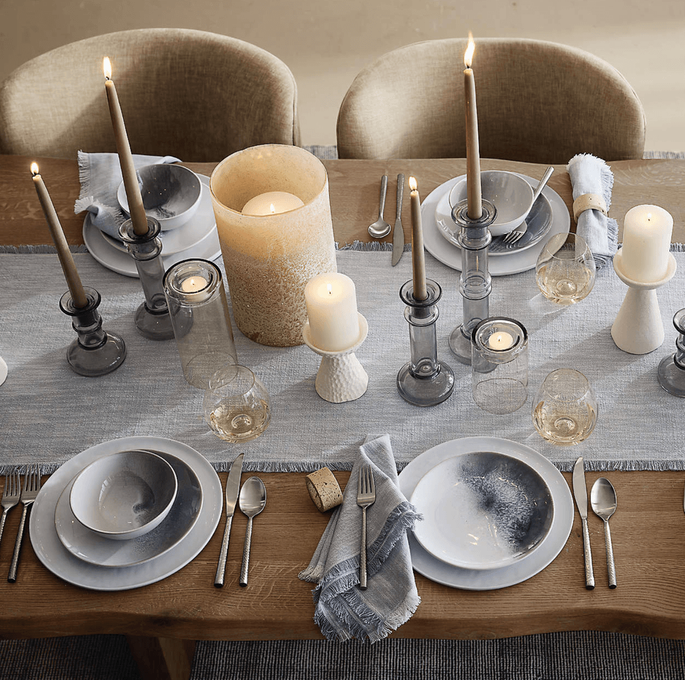 Elegant dinner table with candles, plates, glasses, and silverware on a light blue runner.
