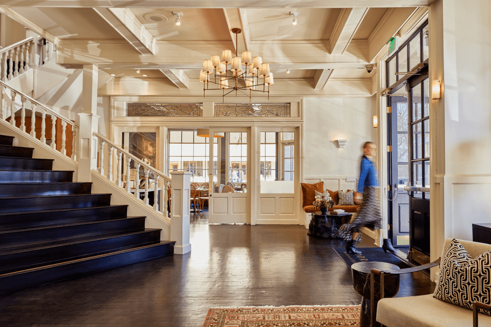 Elegant hotel lobby with staircase, chandelier, and person walking near the entrance.