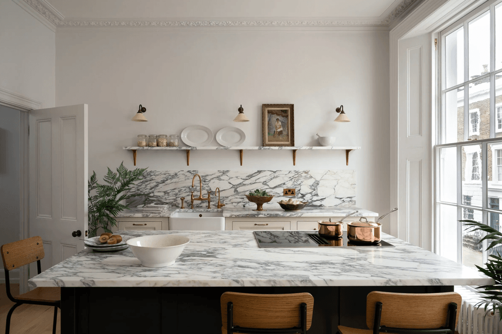Elegant kitchen with marble countertops, copper pots, and large window.