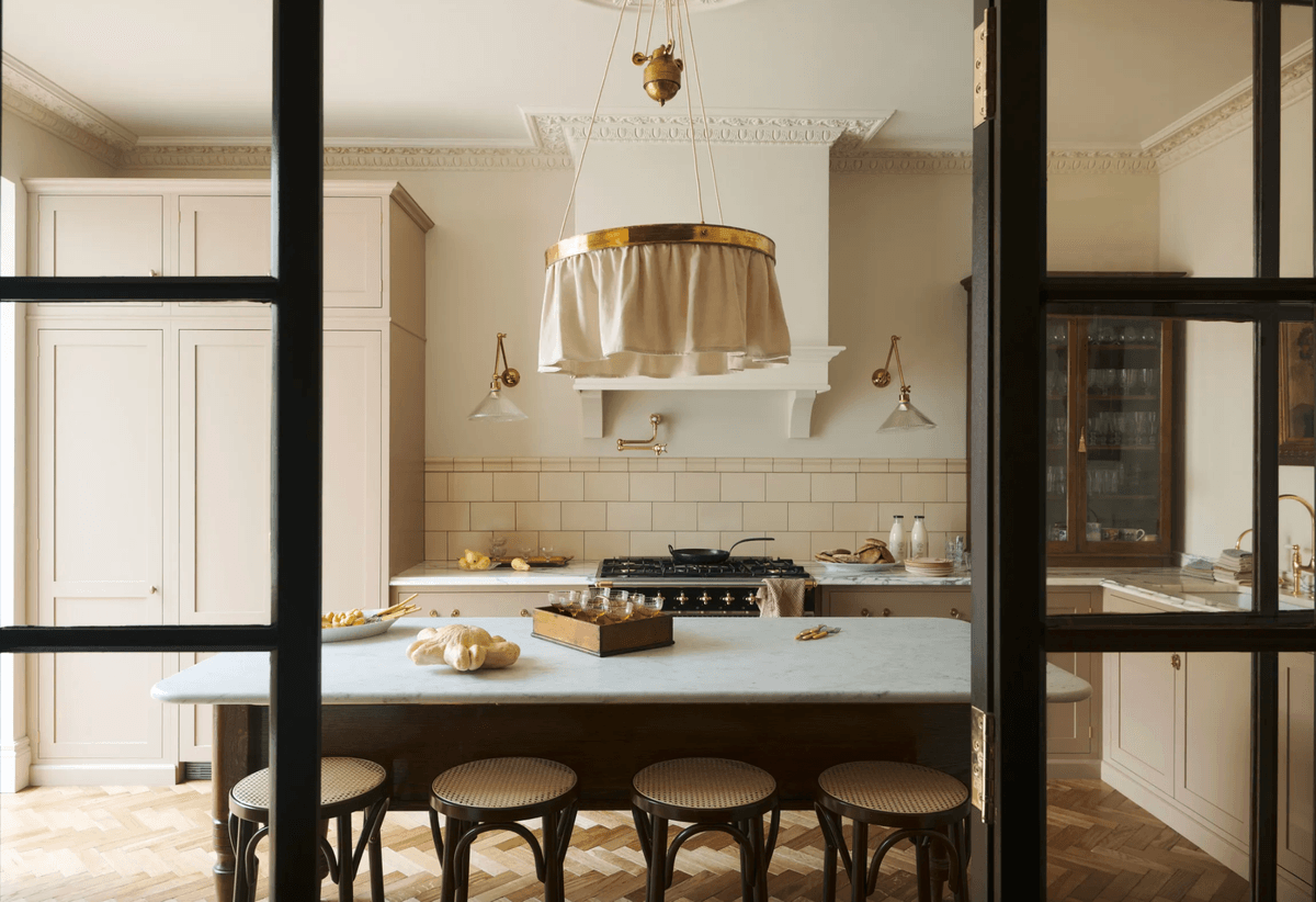 Elegant kitchen with marble island, brass fixtures, four stools, and rustic decor.