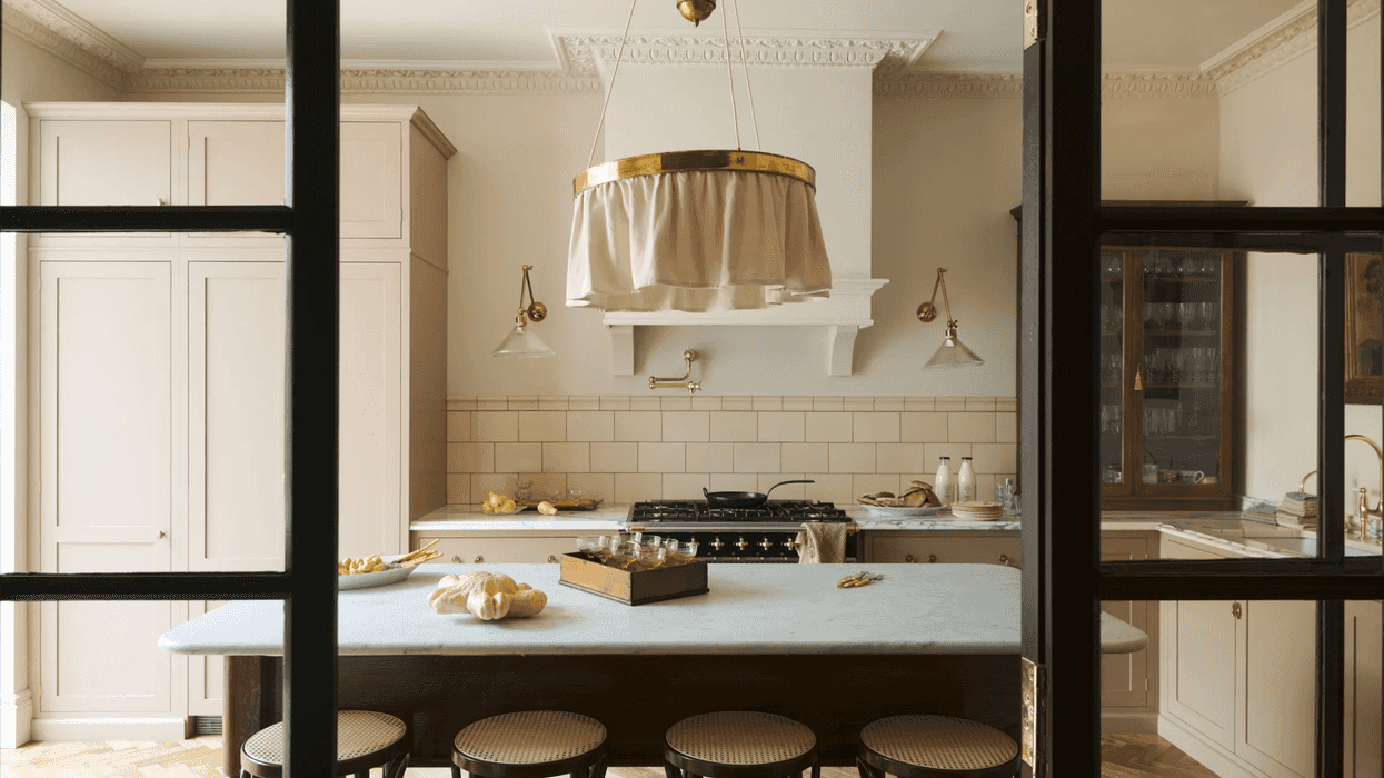 Elegant kitchen with marble island, brass fixtures, four stools, and rustic decor.