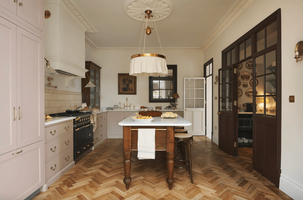 Elegant kitchen with pink cabinets, vintage stove, and herringbone wood flooring.