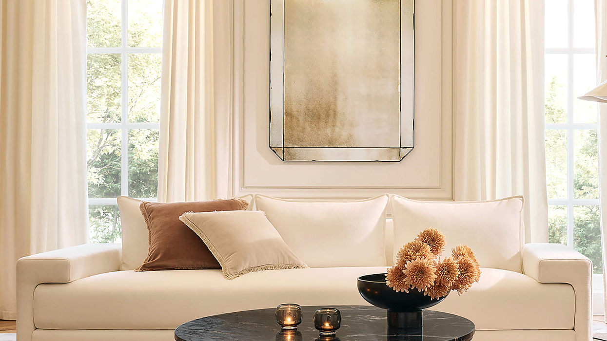 Elegant living room with a white sofa, round table, and large mirror, bathed in natural light.