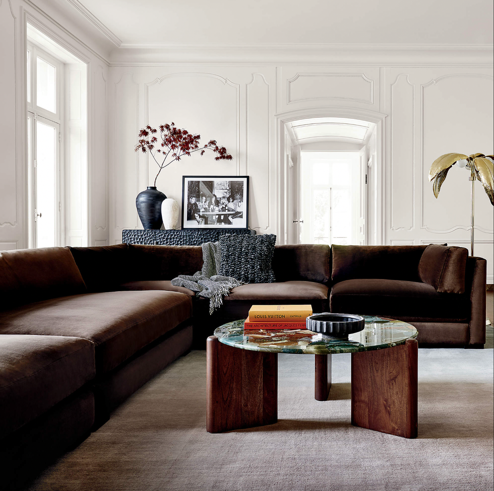 Elegant living room with brown velvet sofa, art, vases, and a round glass coffee table.