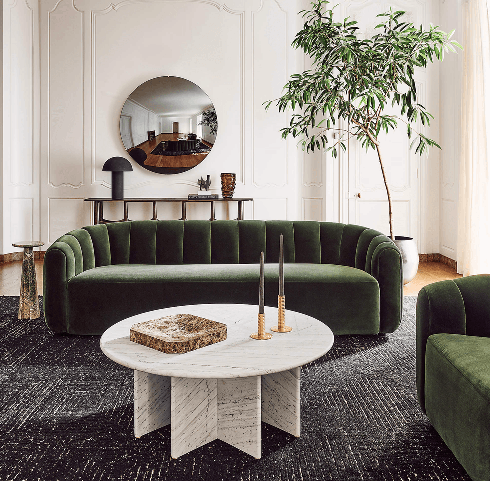 Elegant living room with green velvet sofas, marble tables, and a large round mirror.