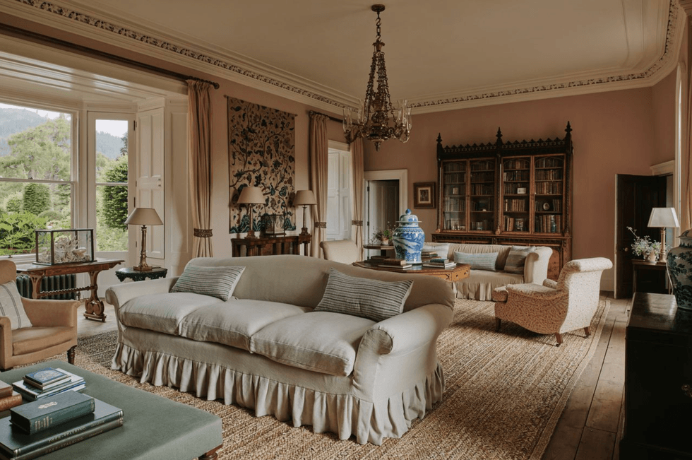 Elegant living room with vintage furniture, ornate chandelier, large windows, and a bookcase.