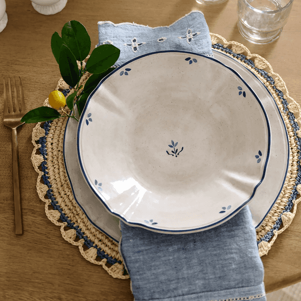 Elegant place setting with plate, blue napkin, lemon branch, and glassware on wooden table.