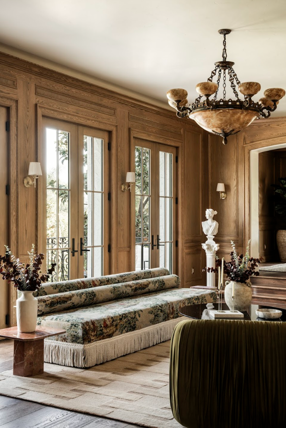 Elegant room with wooden walls, floral sofa, chandelier, and classical bust sculpture.