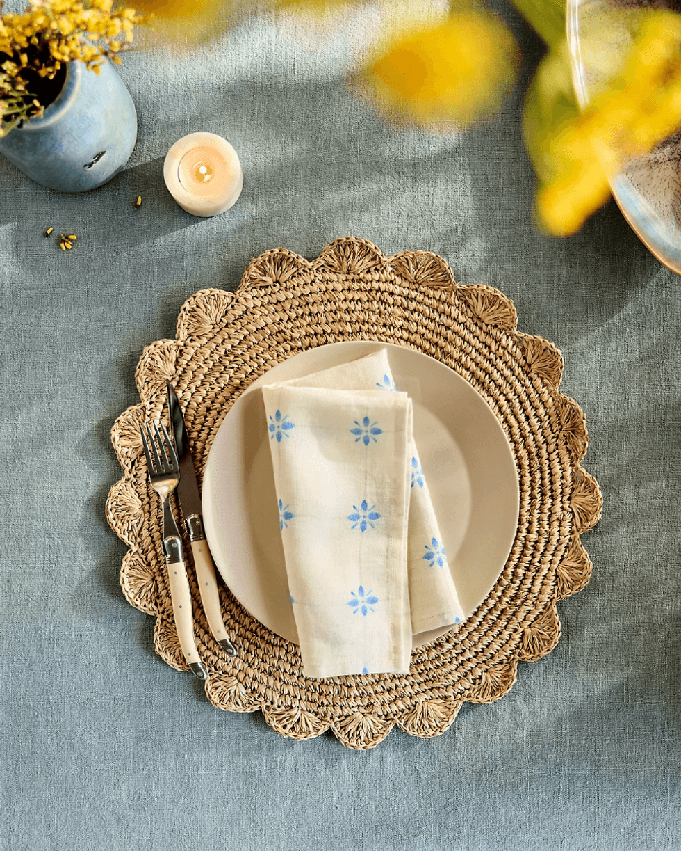 Elegant table setting with floral napkin, candle, and blue tablecloth.