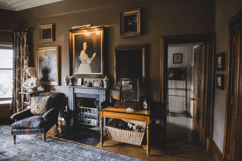 Elegant vintage room with framed portraits, fireplace, and ornate furnishings.