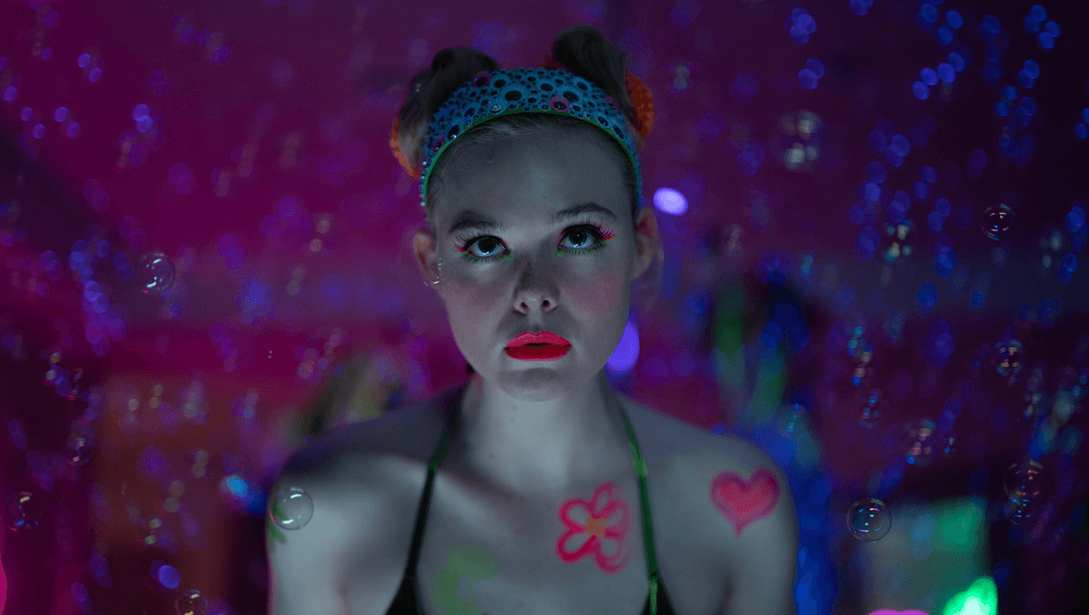 Elle Fanning sporting a neon makeup look and space buns in a dreamy, colorful setting for Apple TV+'s Margo's Got Money Troubles.
