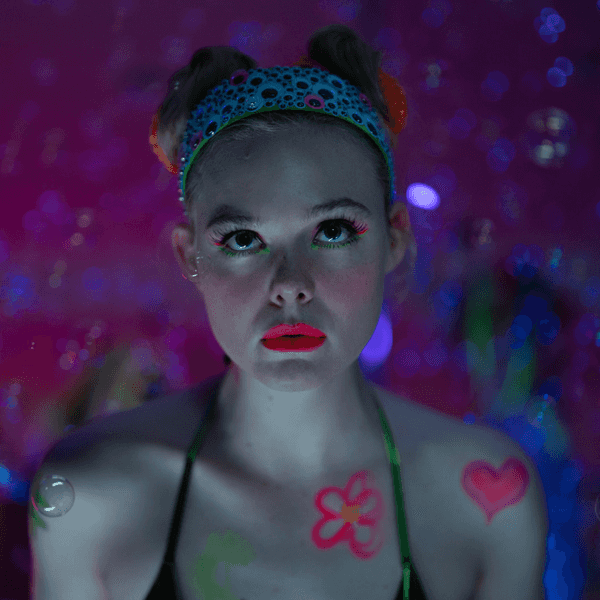 Elle Fanning sporting a neon makeup look and space buns in a dreamy, colorful setting for Apple TV+'s Margo's Got Money Troubles.