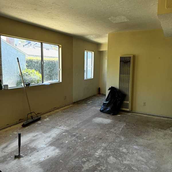 Empty room with bare floor, large windows, and cleaning tools.
