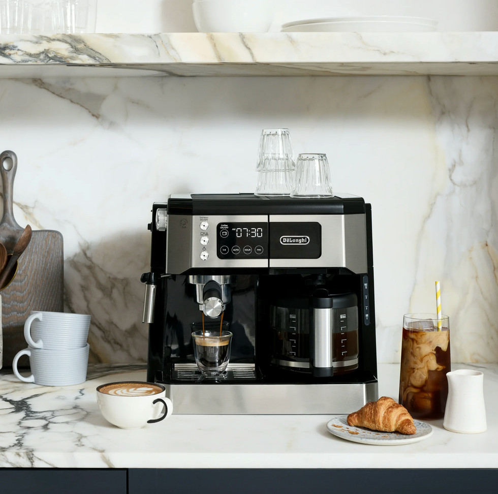 Espresso machine on counter with coffee, croissant, and cups on marble surface.
