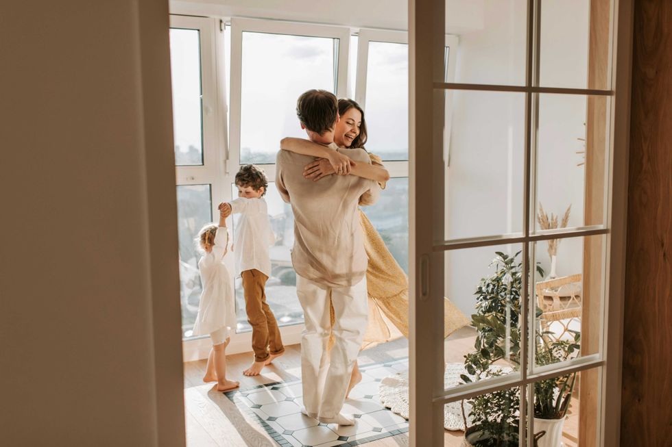 Family dancing joyfully in a bright room with large windows and plants.