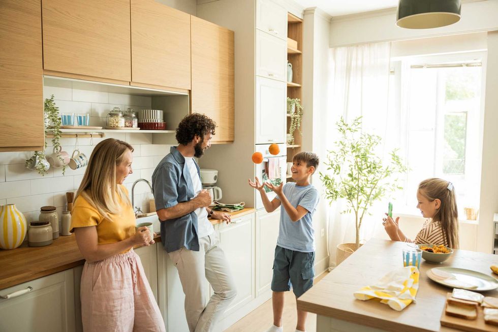 Family enjoying a playful moment in a sunny kitchen, with a boy juggling oranges.