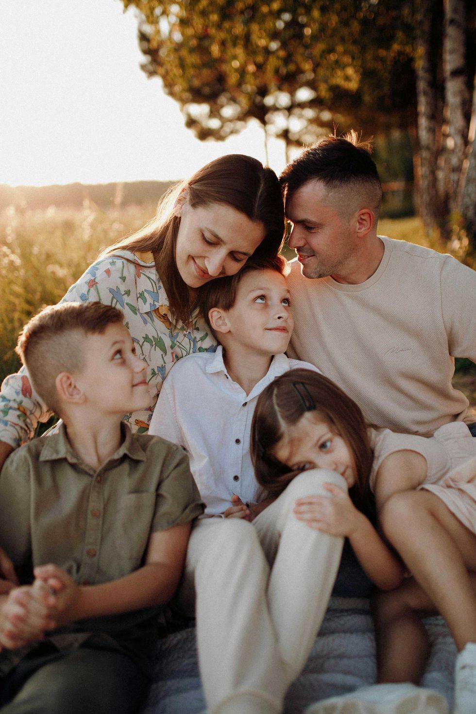 Family sitting together outdoors, smiling and embracing in a sunlit field.