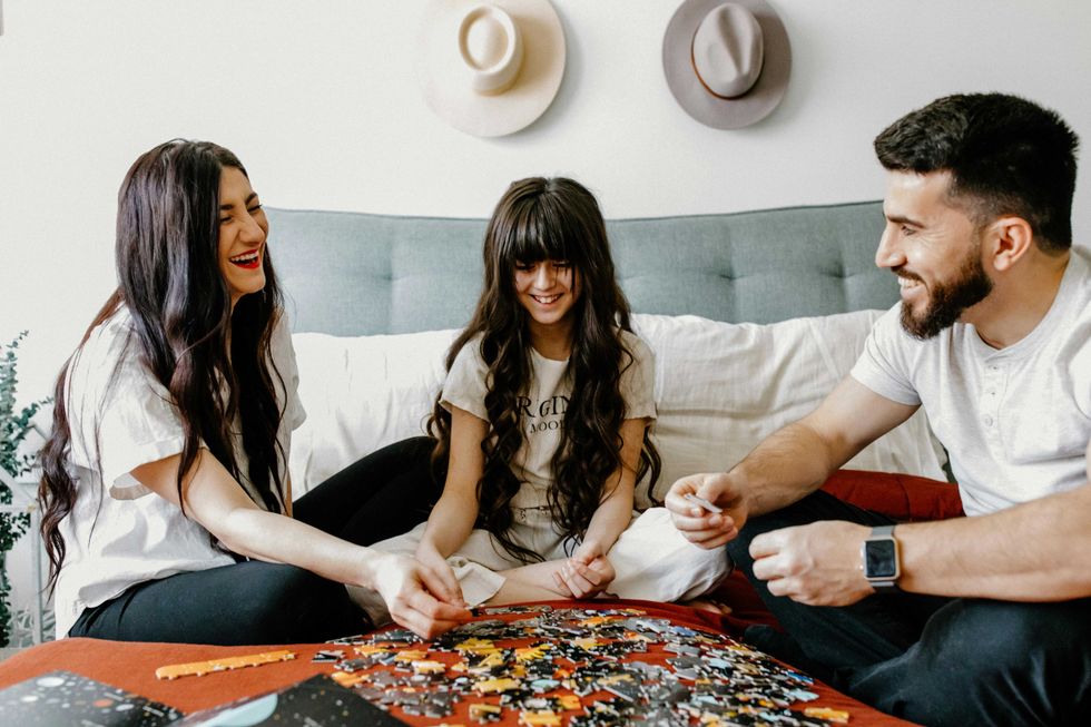 Family smiling and assembling a puzzle on a bed.