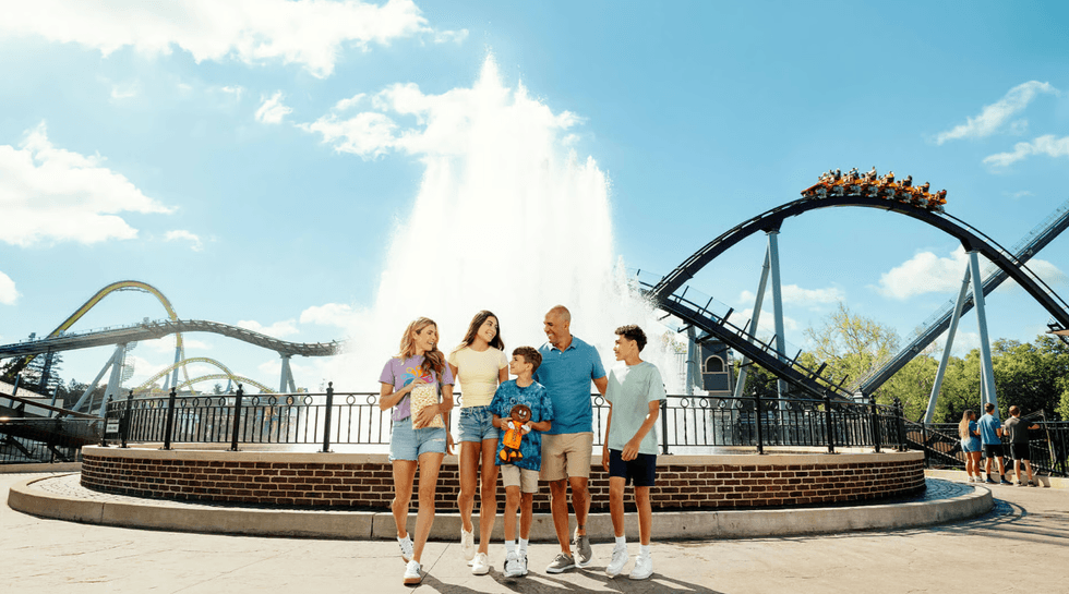 Family walking near amusement park ride and fountain on a sunny day.
