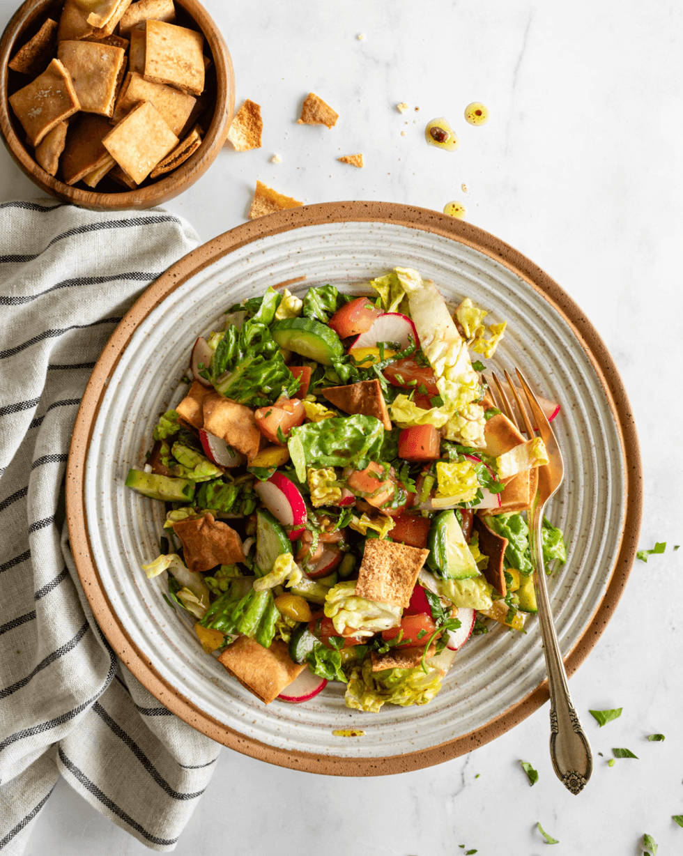 Fattoush salad with pita chips in a large bowl, set on a striped cloth.