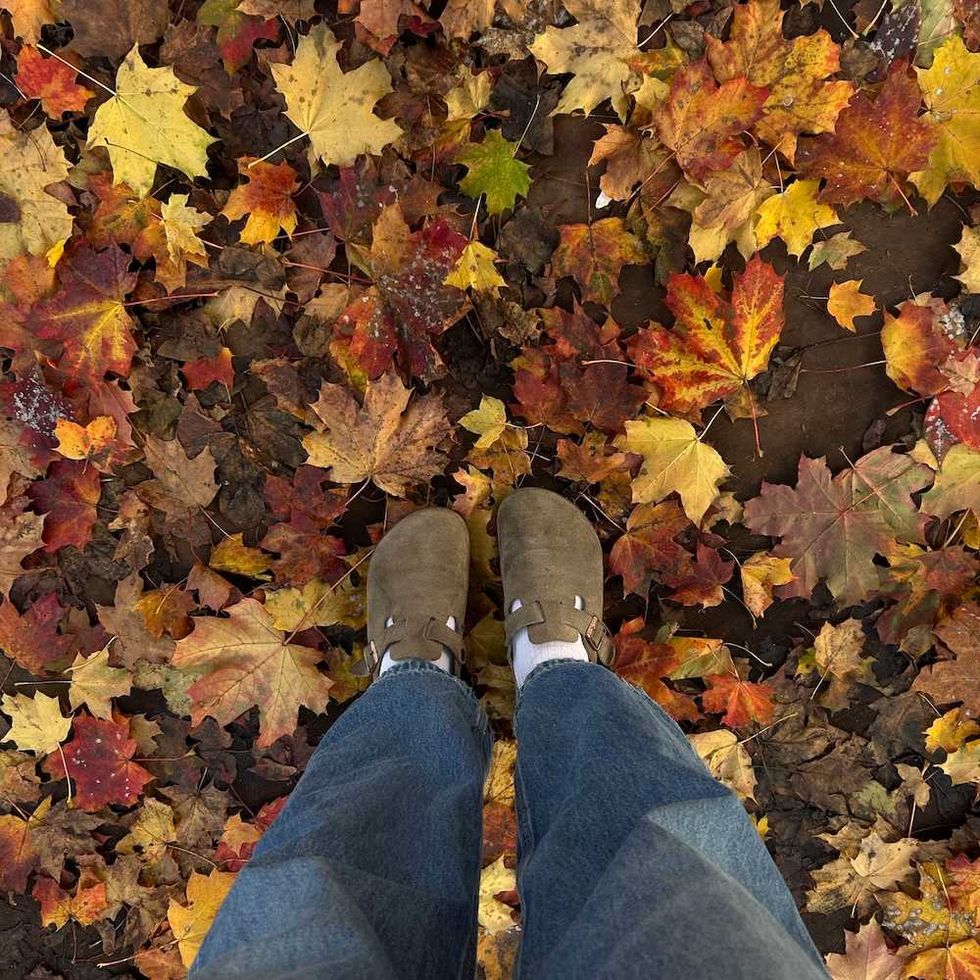 Feet in brown shoes standing on colorful autumn leaves.