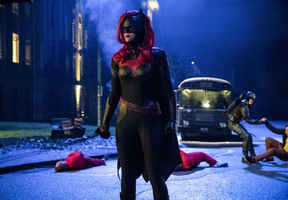 female superhero bat woman in a black and red outfit in the middle of a lamplit street