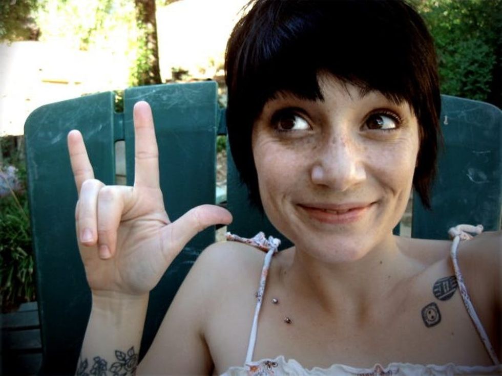 Female with freckles grinning and using an I Love You hand-sign.
