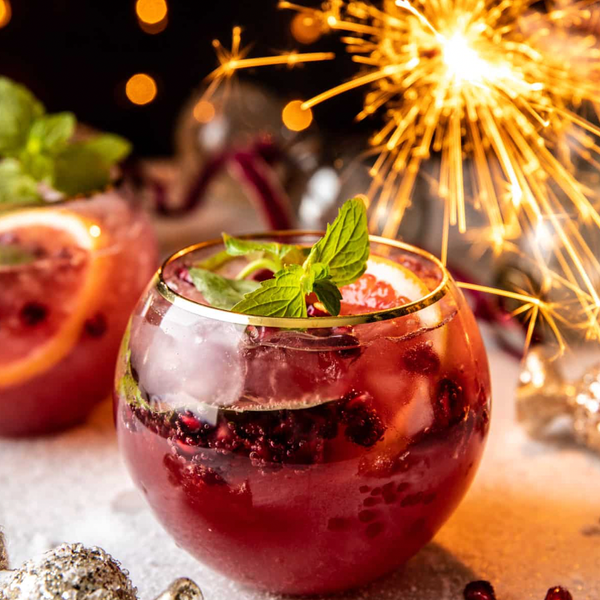 Festive drink with fruit, mint, and sparkler; surrounded by lights and decorations.