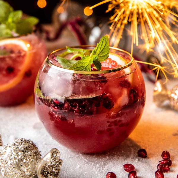 Festive drink with fruit, mint, and sparkler; surrounded by lights and decorations.