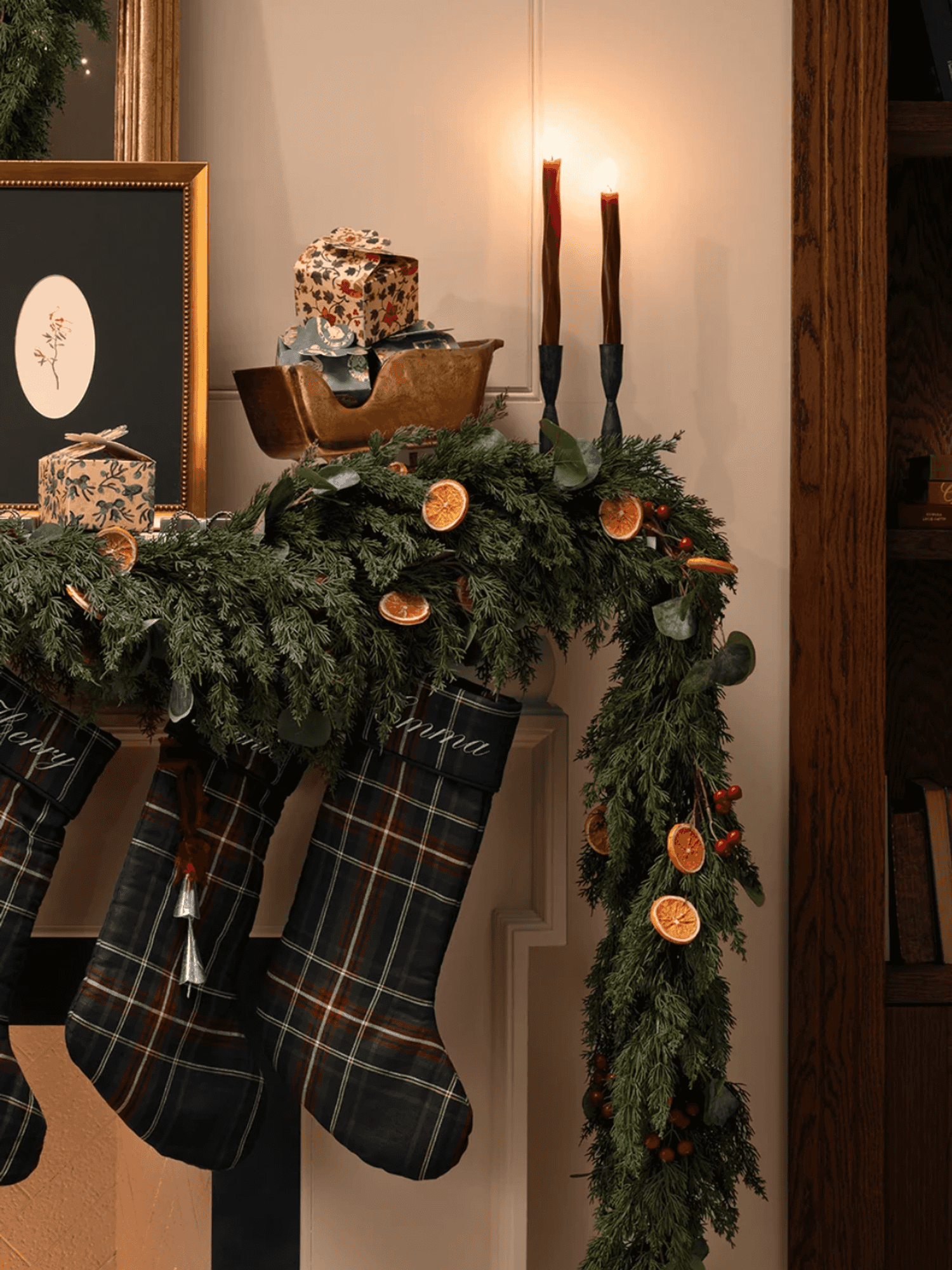 Festive mantel with stockings, greenery, candles, and wrapped gifts.