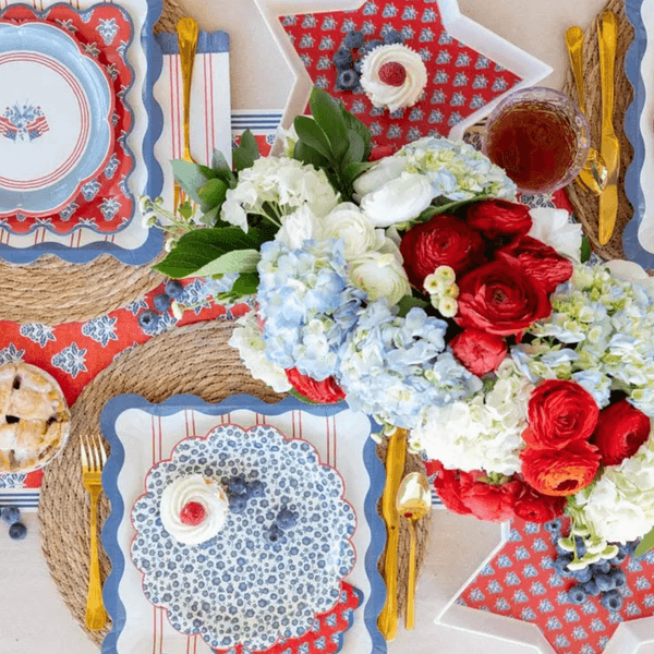 Festive table setting with red, white, and blue decor, flowers, and desserts.