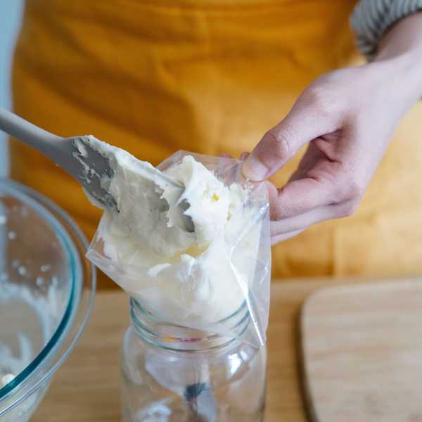 Filling a piping bag with cream using a spatula over a jar.