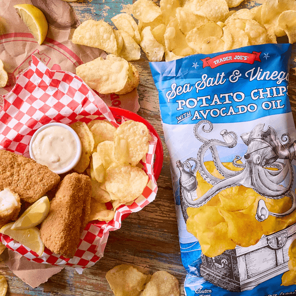 Fish sticks, lemon wedges, chips, and dip next to a bag of sea salt and vinegar chips.