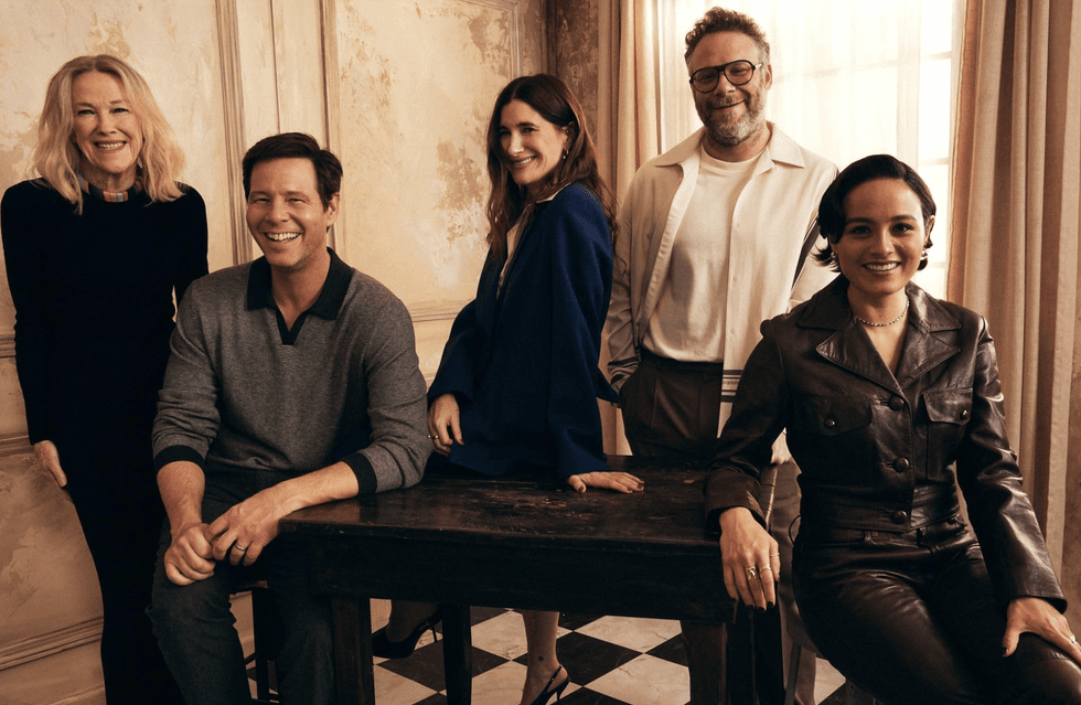 Five people smiling, posing together indoors by a wooden table.