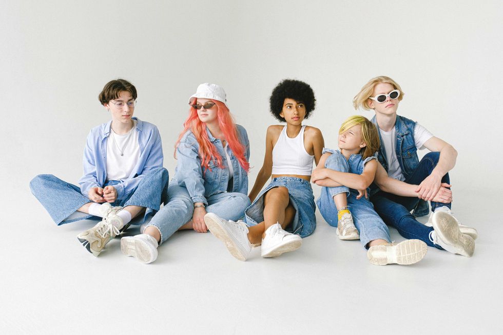 Five stylish people in denim outfits sitting against a plain background.