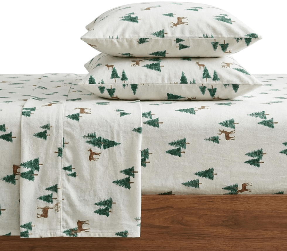 Flannel sheets with green trees and brown deer print on a bed.