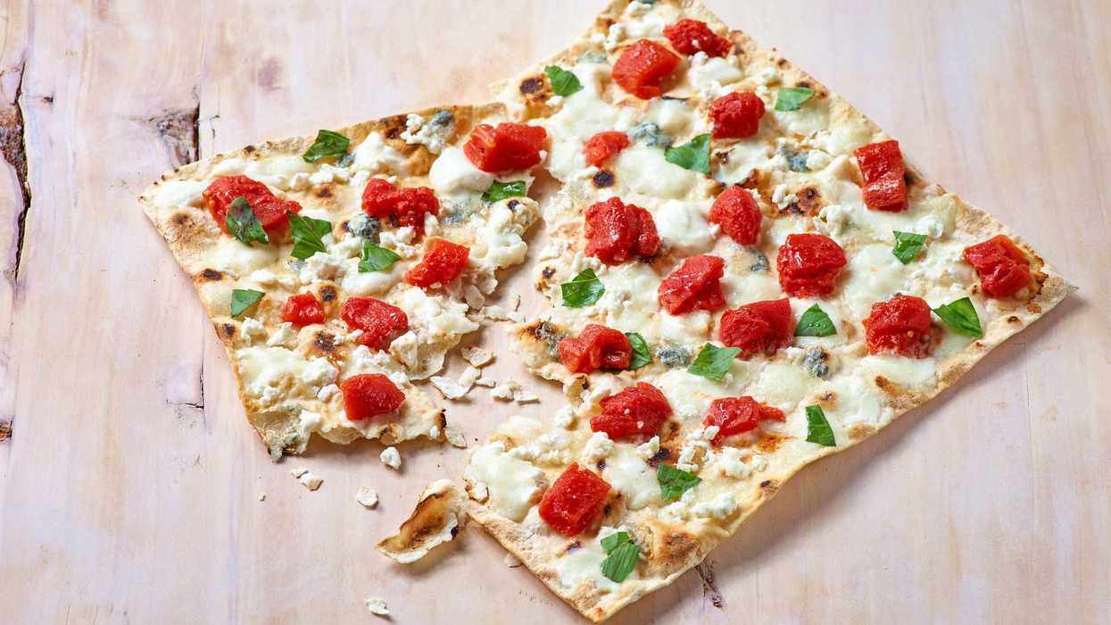 Flatbread pizza with tomatoes, cheese, and basil on a wooden surface.