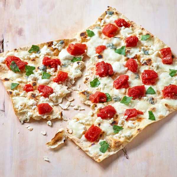 Flatbread pizza with tomatoes, cheese, and basil on a wooden surface.