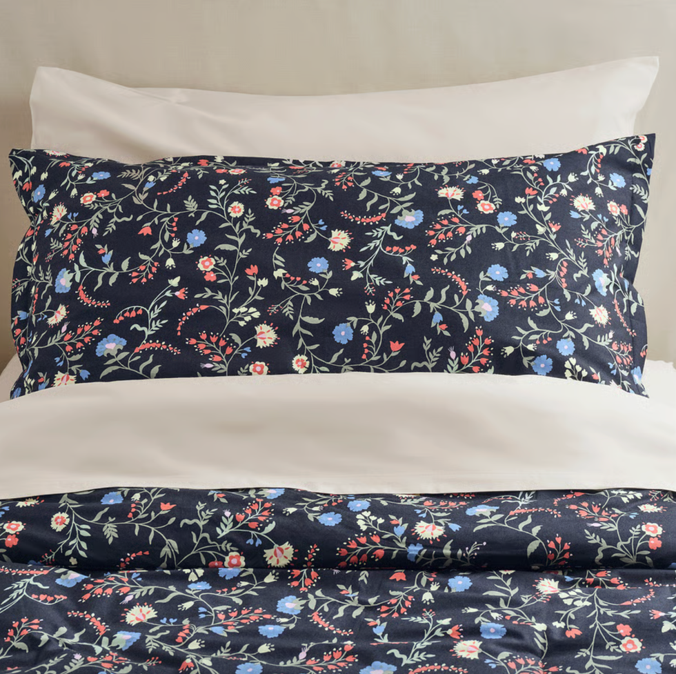 Floral patterned bedding with navy background and multicolored flowers, white pillow behind.