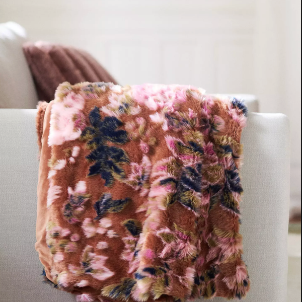 Floral-patterned, plush blanket draped over white sofa in cozy room.