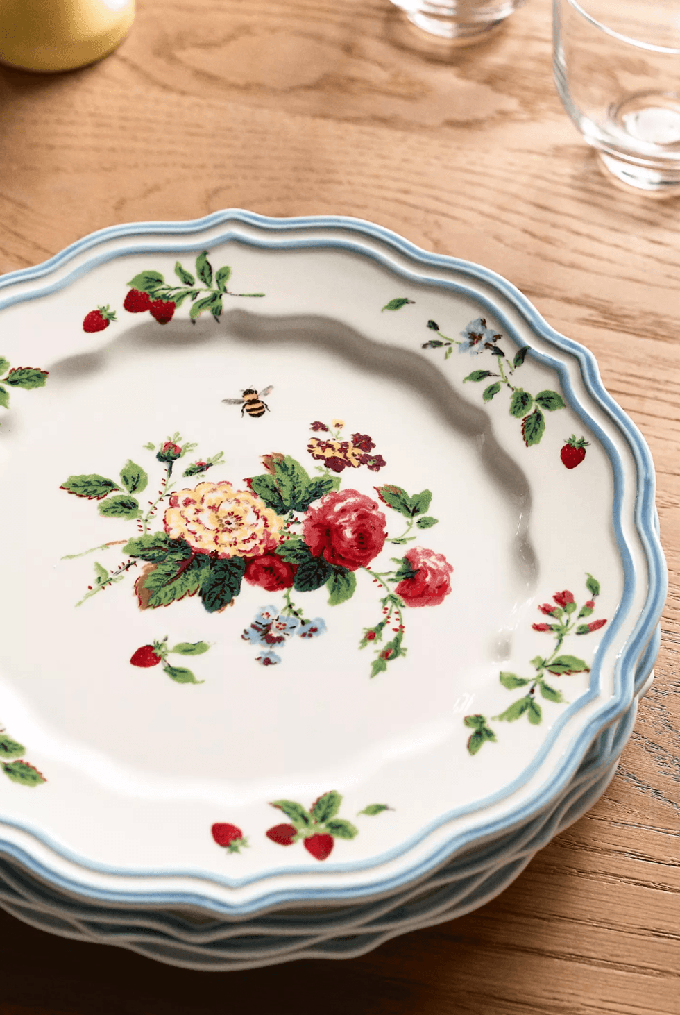 Floral plates with blue rims and bee design on a wooden table.